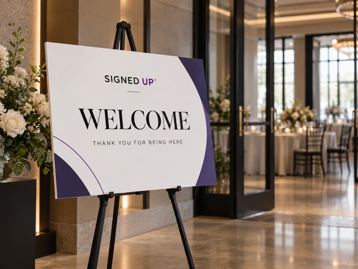 White foam board welcome sign with purple accents on a black easel at an event entrance