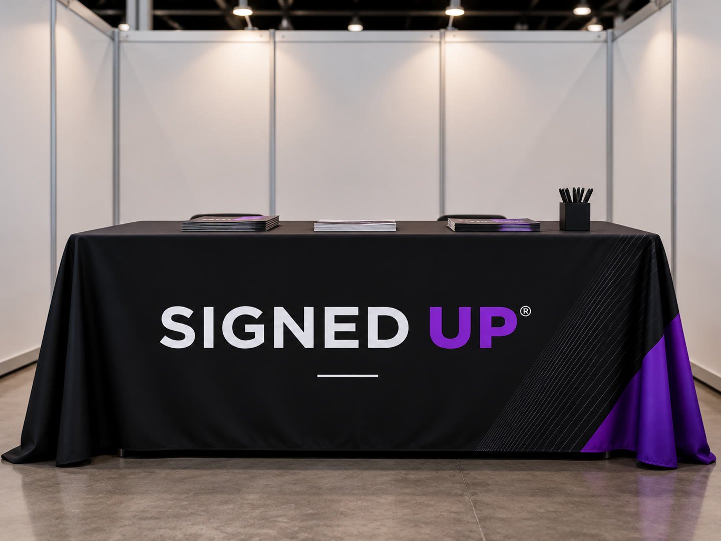 Draped black table cover with a white and purple Signed Up logo at a trade show booth